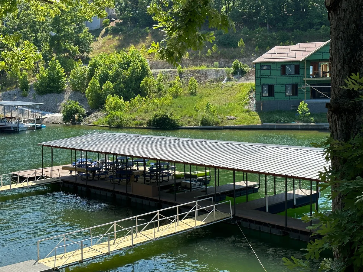 This image presents a serene lakeside scene featuring a spacious dock extending over calm water, with lush greenery in the surroundings. The dock provides ample space for family-friendly activities, including sunbathing, fishing, or just relaxing close to the water. The setting is peaceful yet inviting, ideal for children and parents alike.