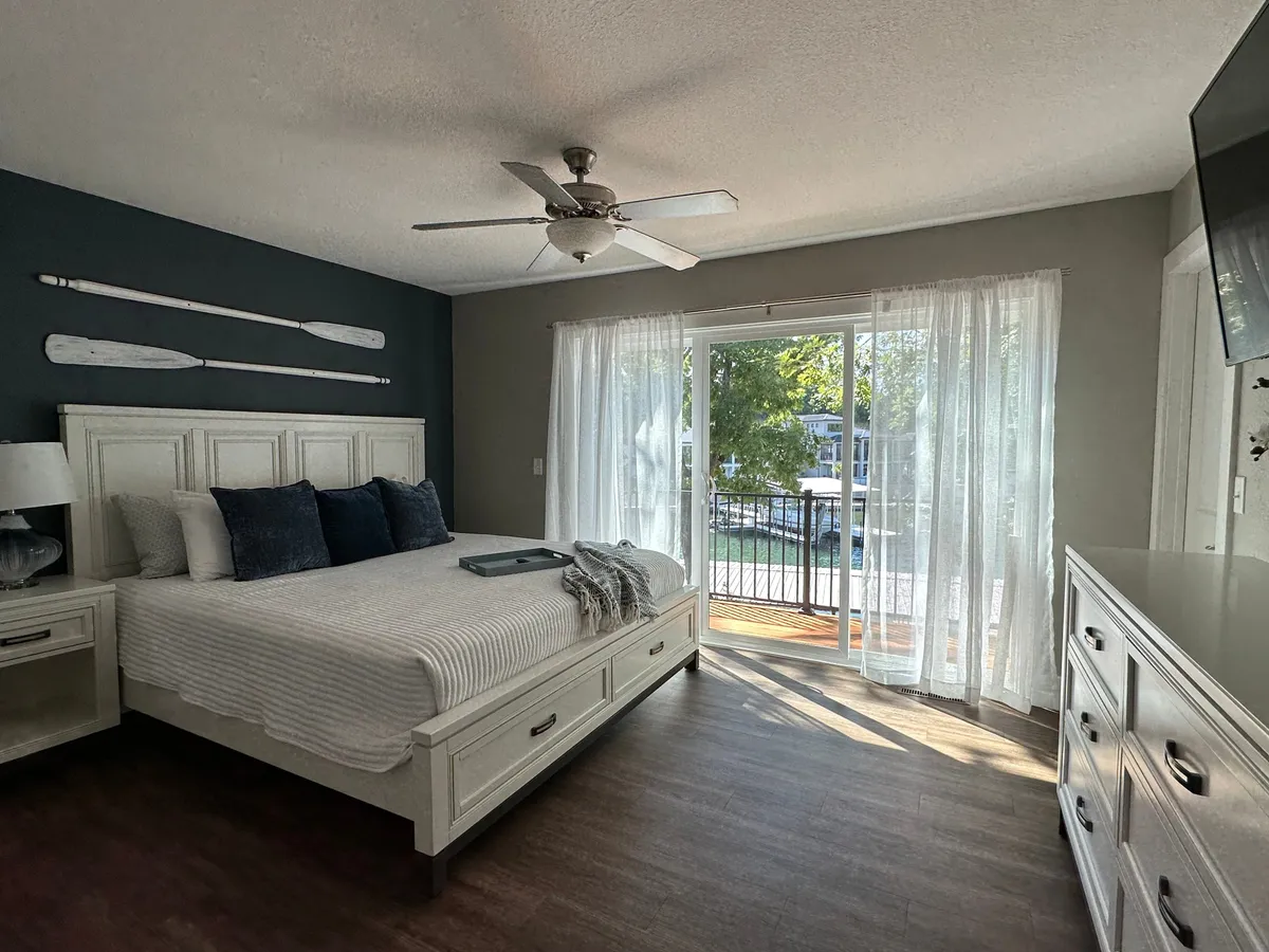 A tranquil bedroom featuring a cozy bed, light streaming through sheer curtains, and decorative oars on the wall. The space exudes calm, inviting couples to relax and enjoy peaceful mornings together while savoring the lakeside ambiance.