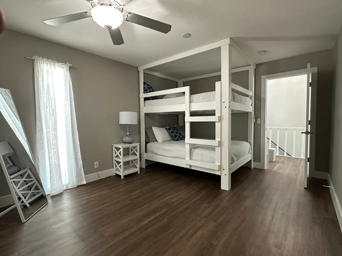 A small, inviting bedroom with a bunk bed, a lamp, and a mirror. The space is cozy, perfect for children or small groups, and emphasizes the potential for quiet nooks and shared memories.