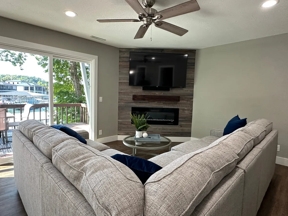 This image shows a cozy living space with a large sectional sofa, a TV mounted on the wall, and a decorative coffee table. The environment feels comfortable and inviting, perfect for relaxing with family or friends in a safe, well-managed setting.