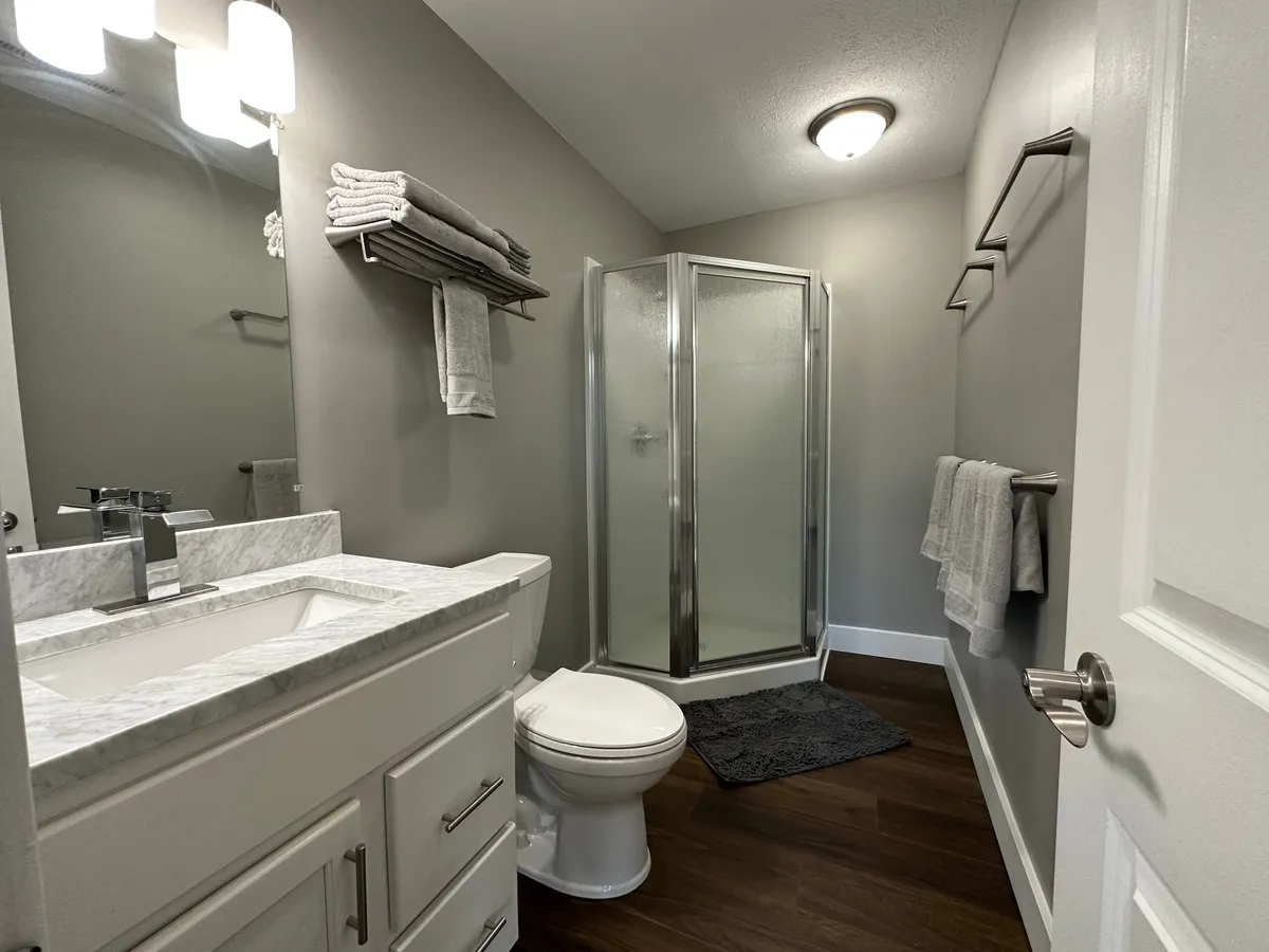 A modern bathroom with a vanity and sink, a glass shower stall, a toilet, and neatly arranged towels. The setting feels fresh and inviting, emphasizing convenience and comfort for morning or evening routines.