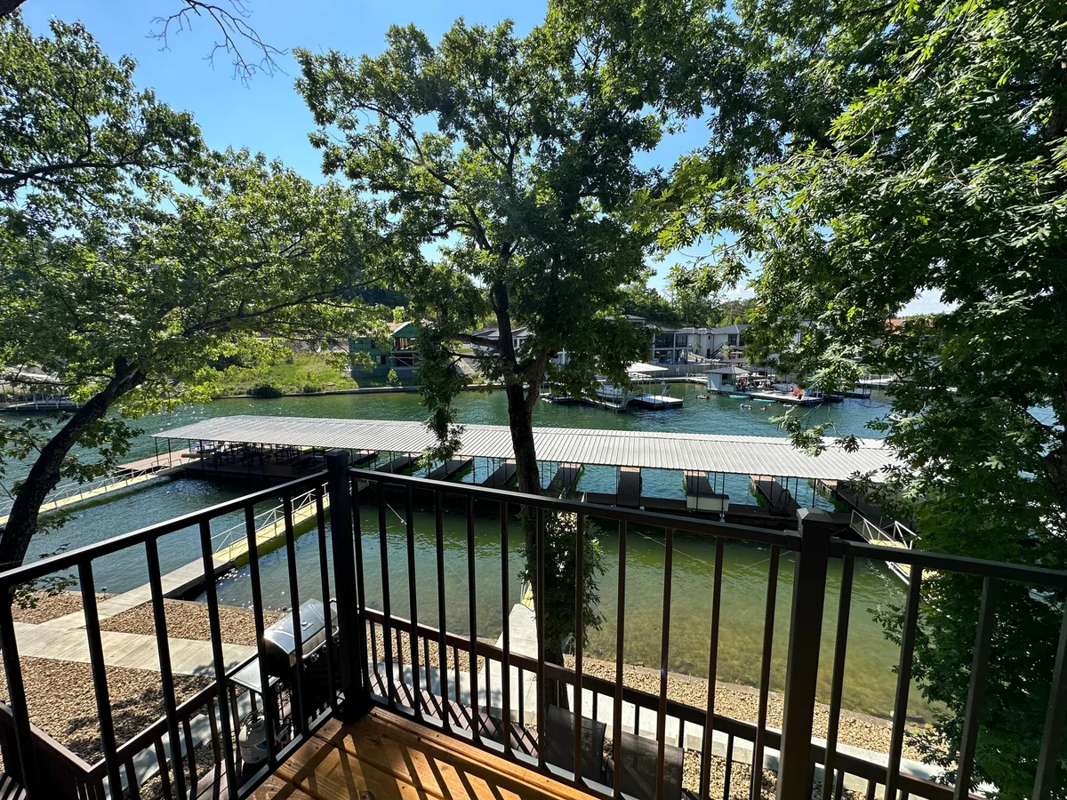 A tranquil dock stretching out over calm, wave-free water, framed by lush trees. The dock includes open areas ideal for lounging or sunbathing. The scene exudes peace but also invites activities like boating and fishing. The expansive water and trees emphasize the lakeside setting.