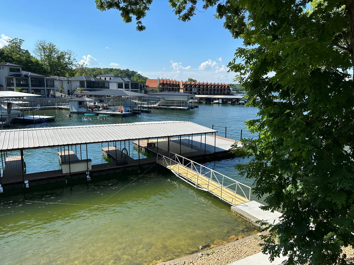 A wide waterfront scene featuring multiple docks and boathouses, with people enjoying the water and relaxing by the shore. The area looks lively yet serene, hinting at both social activity and the opportunity for peaceful moments by the lake.