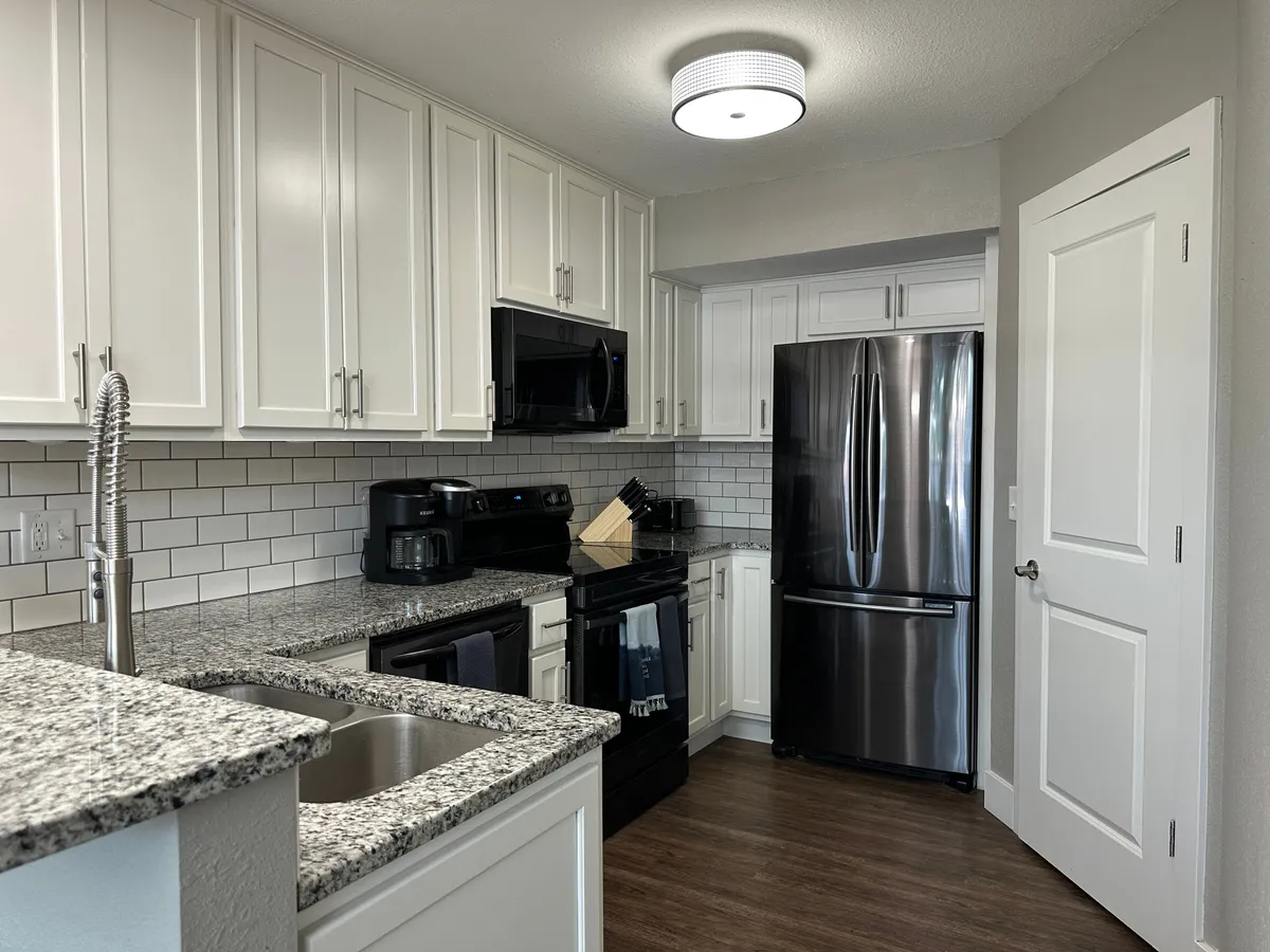 A modern, fully stocked kitchen featuring granite countertops, stainless steel appliances, crisp white cabinetry, and a stylish subway tile backsplash. The space is designed for both functionality and aesthetics, providing ample room for cooking, entertaining, and gathering.