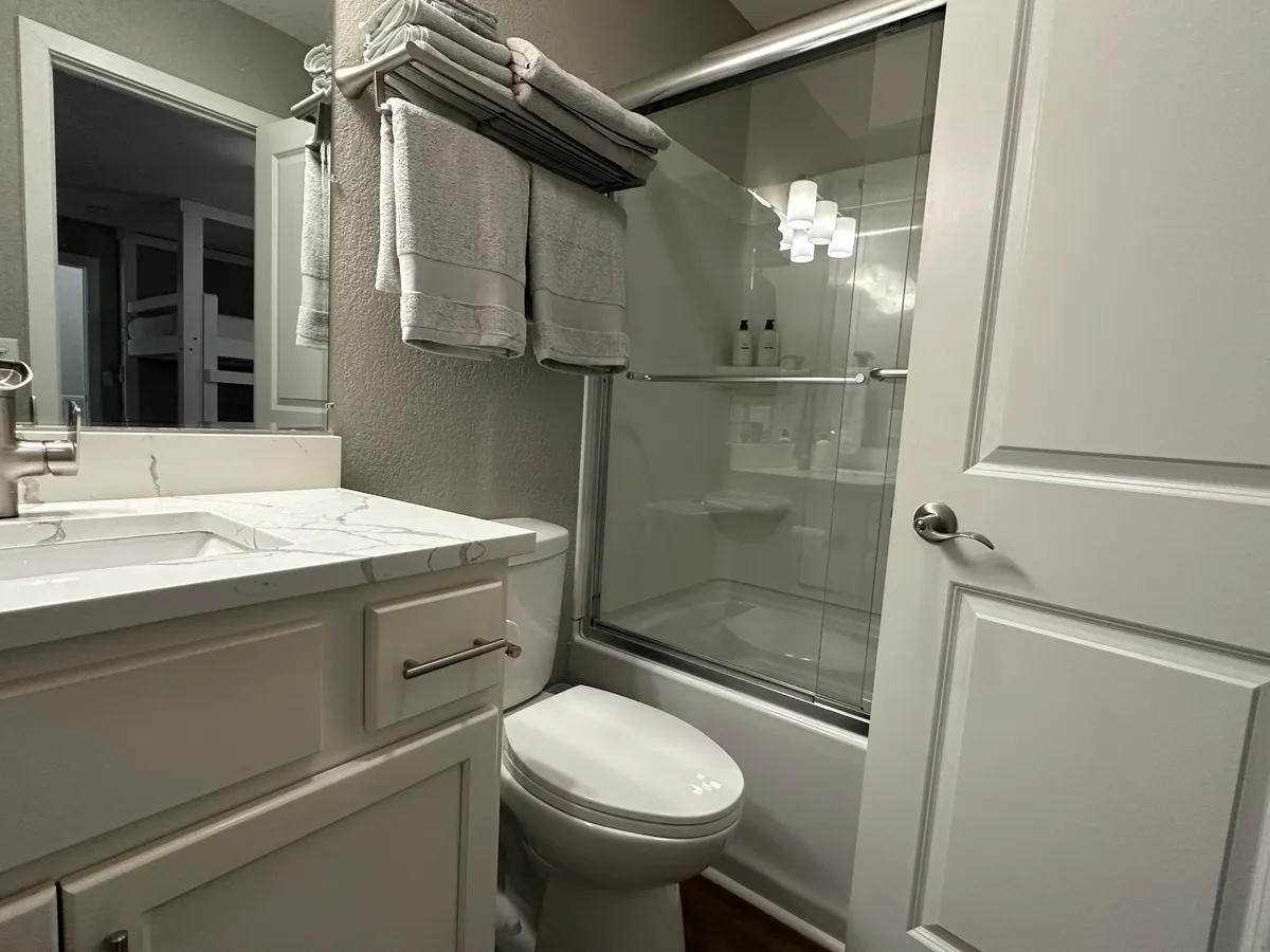 A sleek bathroom with a marble countertop, a spacious glass shower enclosure, and neatly arranged towels. The serene color palette and natural light offer a spa-like, calming environment for unwinding after a day of lakeside adventures.