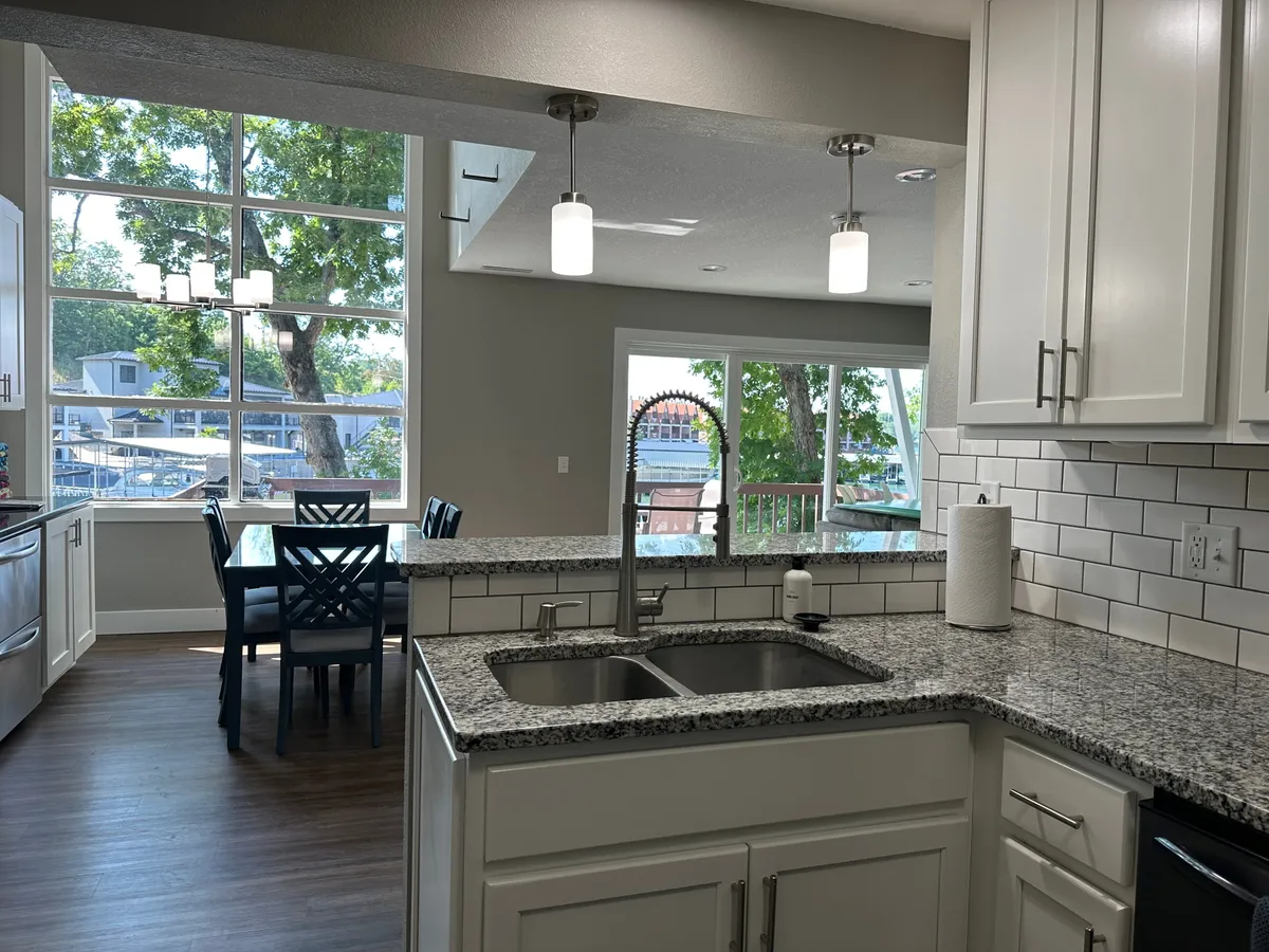 A roomy kitchen and dining area with a granite countertop and a large dining table, flanked by expansive windows. The space exudes a sense of openness, perfect for cooking, entertaining, and gathering friends before heading out.