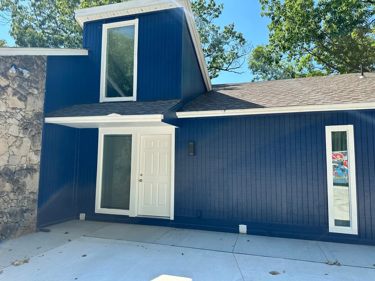 The image presents the home's blue exterior walls, large windows, and prominent front door—a clear entry point that sets the tone for secure and private condo-style living. The scene feels welcoming and modern, embodying the sense of arriving at a thoughtfully managed property.